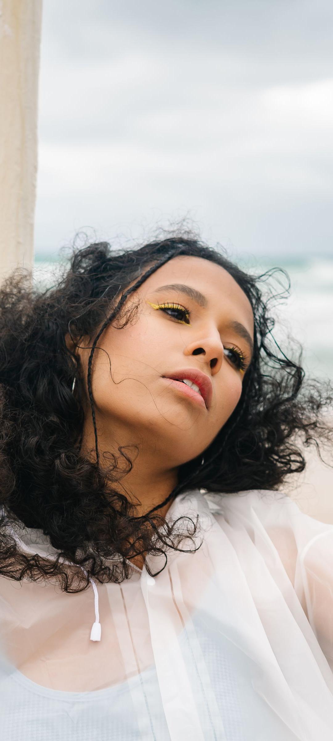 Mujer con el cabello rizado al viento en una playa en verano